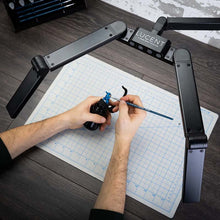 Game Envy LUCENT Art and Hobby Light with adjustable LED panels illuminating miniature painting on a cutting mat.